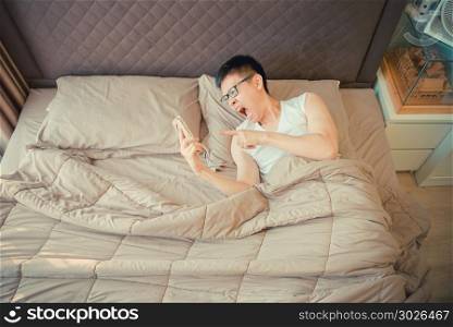 Angry Asian man blaming on the phone on bed