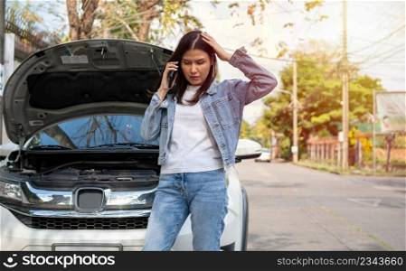Angry Asian woman and using mobile phone calling for assistance after a car breakdown on street. Concept of vehicle engine problem or accident and emergency help from Professional mechanic