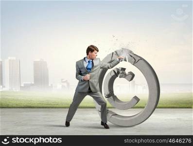 Angry businessman crashing stone trademark with karate kick. Copyright concept