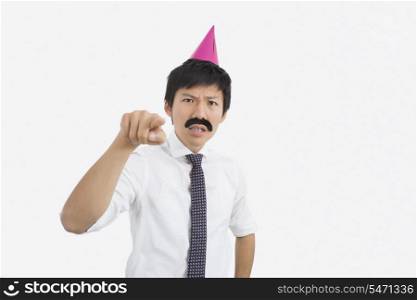 Angry businessman wearing party hat pointing in office