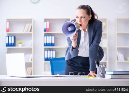 Angry businesswoman yelling with loudspeaker in office