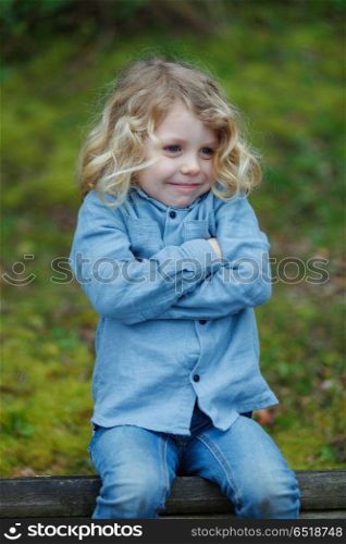 Angry child with long blond hair crossing his arms . Angry child with long blond hair crossing his arms sitting on a bench