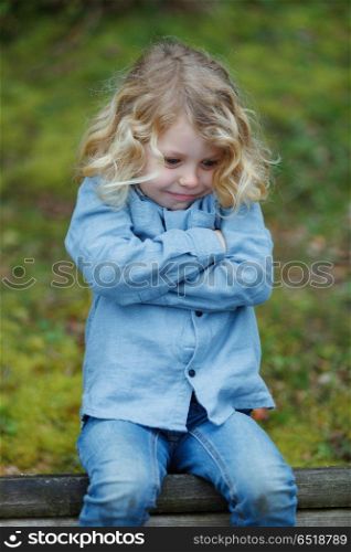 Angry child with long blond hair crossing his arms . Angry child with long blond hair crossing his arms sitting on a bench