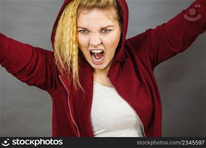Angry energetic motivated blonde woman wearing sporty outfit, red hoodie. Female having screaming face expression. Angry sporty woman screaming