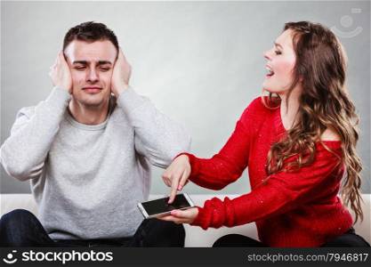 Angry furious wife shouting at husband showing text messages from lover mistress on his mobile phone. Outraged girlfriend find out about boyfriend affair romance betrayal. Cheating man covering ears.