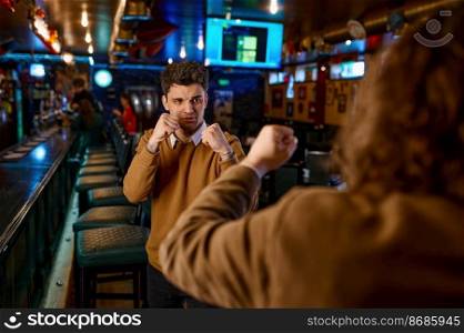 Angry male friends fighting at sport bar. Selective focus on fury guy clenching fist. Aggressive soccer spectators boxing in pub. Angry male friends fighting at sport bar