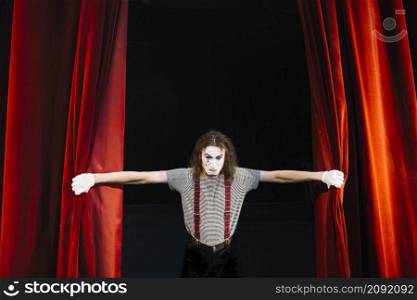 angry male mime artist holding red curtain