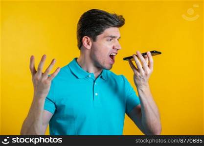 Angry modern man in blue t-shirt screaming down his mobile phone. Stressed and depressed man on yellow background. Angry modern man in blue t-shirt screaming down his mobile phone. Stressed and depressed man on yellow background.