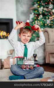 Angry upset little boy with a gift, toy train, under the Christmas tree on a New Year&rsquo;s morning. A time of miracles and fulfillment of desires. Merry Christmas.. Angry upset little boy with a gift, toy train, under the Christmas tree on New Year&rsquo;s morning. Time to fulfill wishes.