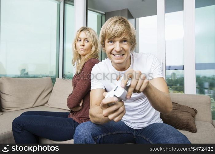 Angry woman looking at man play video game in living room at home