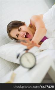 Angry woman stretching to turn off alarm clock
