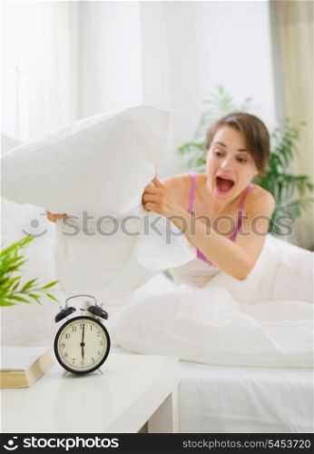 Angry woman trying to break alarm clock by pillow