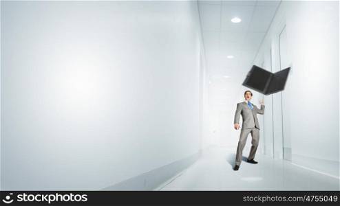 Angry young businessman in rage throwing laptop