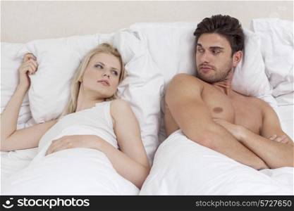 Angry young couple looking at each other in bed