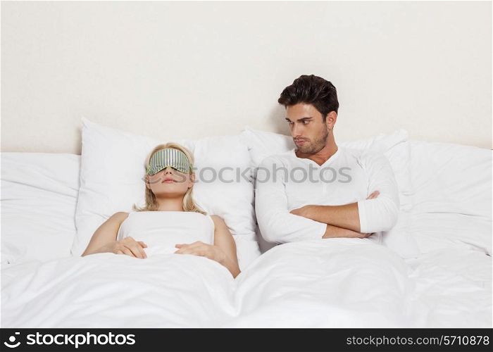 Angry young man looking at woman sleeping in bed