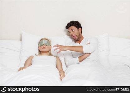 Angry young man teasing sleeping woman in bed