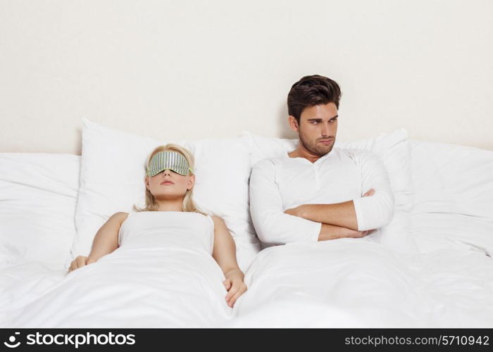 Angry young man with woman sleeping in bed