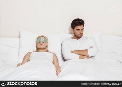 Angry young man with woman sleeping in bed