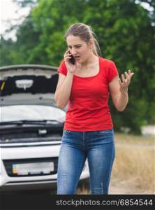 Angry young woman shouting in mobile phone because of the broken car