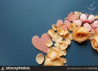 angular frame wafer hearts and rose petals on a blue background. heart waffles and rose petals