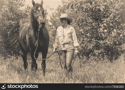 Animal and human love, equine concept. Western woman walking on green meadow or forest with horse. Western woman walking on green meadow with horse