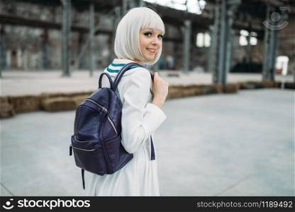 Anime style blonde girl with backpack. Cosplay, japanese culture, doll in dress on abandoned factory