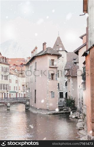 Annecy, France in winter snowstorm. Historical buildings along canal in the city center in snowy weather. Magic Christmas mood. Monochromatic neutral tones with natural light
