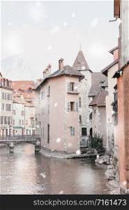 Annecy, France in winter snowstorm. Historical buildings along canal in the city center in snowy weather. Magic Christmas mood. Monochromatic neutral tones with natural light