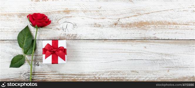 Anniversary background with a single red rose and wrapped gift box on white rustic wood