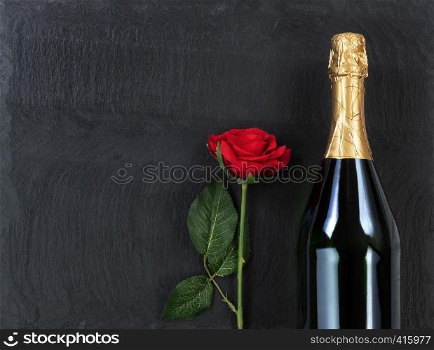 Anniversary background with red rose and champagne on natural black slate stone