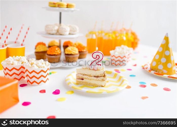 anniversary, celebration and festive concept - piece of cake with candle in shape of number two on plate at birthday party. piece of cake on plate at birthday party