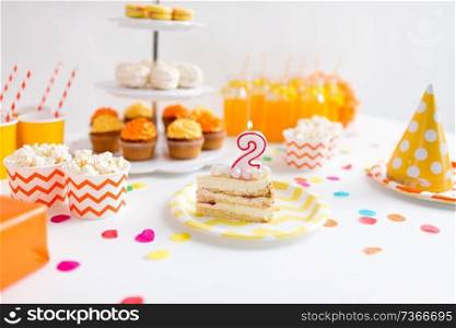 anniversary, celebration and festive concept - piece of cake with candle in shape of number two on plate at birthday party. piece of cake on plate at birthday party