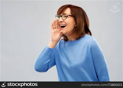 announcement and old people concept - senior woman in glasses calling over grey background. senior woman in glasses calling over grey