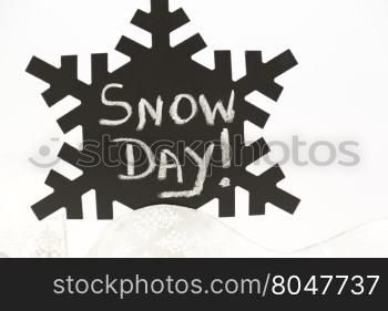 Announcement of Snow Day! written on old, dusty black snowflake against white background and with silver ribbon below.
