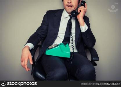Annoyed businessman is sitting in an office chair and is on the phone