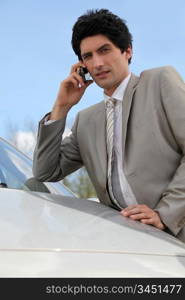 Annoyed businessman talking on his mobile phone by his car