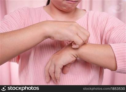 Annoyed middle-aged woman scratching itch on her arm from itchy dry skin, eczema, dermatitis, allergy, psoriasis. Health care and skin disease concept.