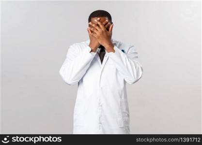 Annoyed, pissed-off african-american male doctor trying avoid annoying patient, cover face with hands hope he dont see me, feel tired or embarrassed, physician suffer fatigue, emotional burnout.. Annoyed, pissed-off african-american male doctor trying avoid annoying patient, cover face with hands hope he dont see me, feel tired or embarrassed, physician suffer fatigue, emotional burnout