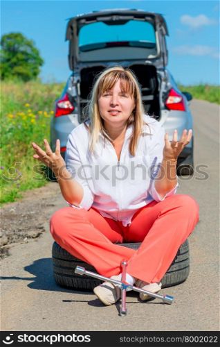 annoyed woman sitting on the bursting of the wheel and waiting for help