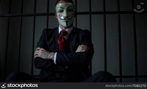 Anonymous hacker in prison with arms crossed