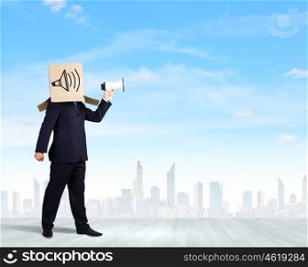 Anonymous message. Businessman wearing carton box on head and speaking in megaphone