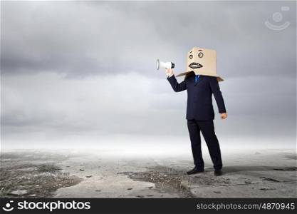 Anonymous message. Businessman wearing carton box on head and speaking in megaphone