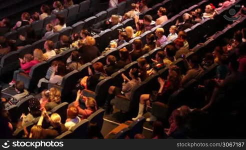 Anonymous people applaud at the theatre performance. Shot from back, no visible faces. High angle.