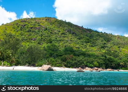 Anse Lazio with rocky granite coastline on the beach and forest on the mountain.