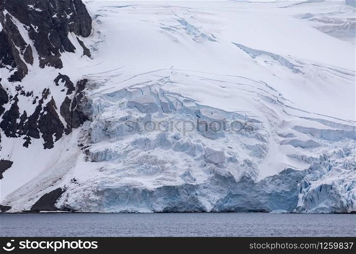 Antarctic glacier with white ice falls off into calm blue sea