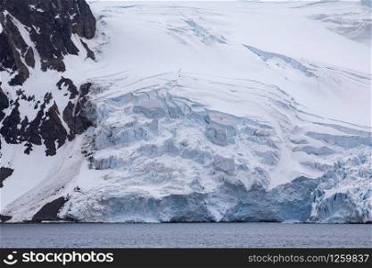 Antarctic glacier with white ice falls off into calm blue sea