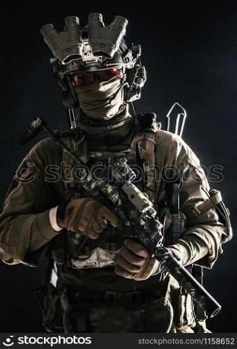 Anti-terrorist squad fighter, army elite forces soldier in combat uniform and tactical ammunition, armed mini submachine gun, wearing night-vision device, low key studio portrait on black background. Anti-terrorist squad equipped fighter soldier in darkness