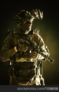 Anti-terrorist squad fighter, army elite forces soldier in combat uniform and tactical ammunition, armed mini submachine gun, wearing night-vision device, low key studio portrait on black background. Anti-terrorist squad equipped fighter soldier in darkness