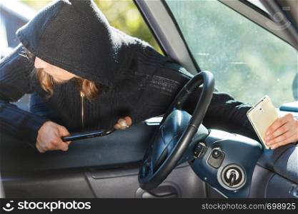 Anti theft system problem concept. Burglar thief man wearing black clothes breaking into car and stealing smartphone. Burglar thief breaking into car stealing smartphone