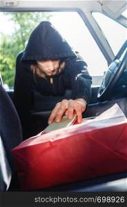 Anti theft system problem concept. Burglar thief man wearing black clothes breaking into car, stealing smartphone and red shopping bag. Burglar thief stealing smartphone and bag from car